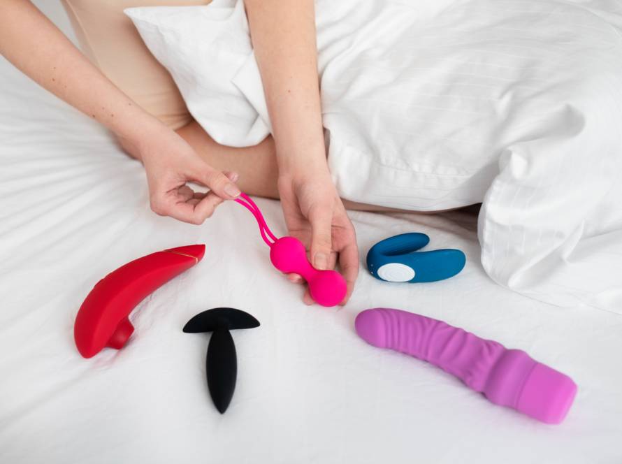kobieta trzyma dildo i inne zabawki erotyczne na łóżku