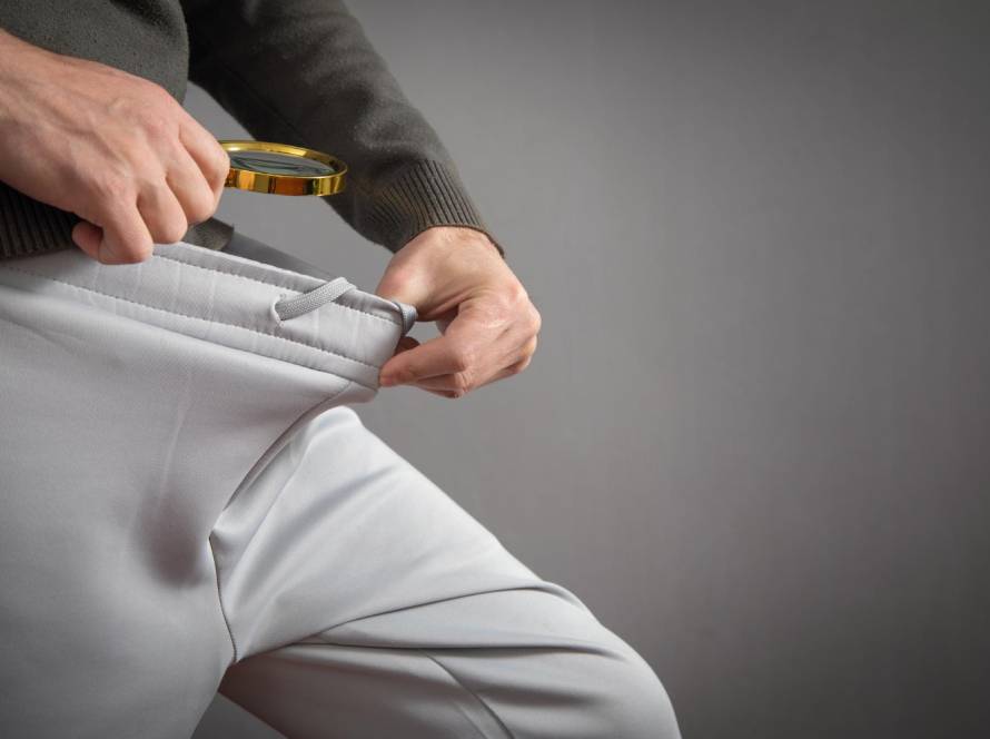 Jak działa pompka do penisa? Powiększanie penisa i leczenie erekcji 1 Mężczyzna sprawdza czy jego penis został powiększony po użyciu pompki do penisa. Podnosi spodnie i zagląda z lupą.